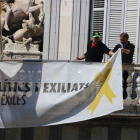 Dos treballadors retiren les pancartes del balcó del Palau de la Generalitat.