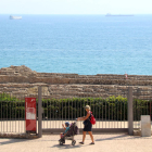 Pla general d'una dona passant amb el carret d'un nadó per davant de la reixa de l'amfiteatre romà de Tarragona, tancat al públic de forma provisional. Imatge del 27 de setembre del 2019