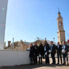 Foto de familia en la terraza del Museu Casteller de Catalunya en Valls, en una visita de obras con la consellera de Cultura, Laura Borràs, con el campanario de la ciudad en el fondo.