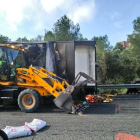 Imatge del camió incendiat, amb les fruites i verdures al terra i operaris treballant en la retirada de la mercaderia.