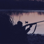 Pla general d'un caçador preparat per disparat en una llacuna, de nit.