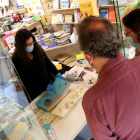 La librera de Al·lots, Paula Jarrín, recomienda libros infantiles a dos clientes desde la entrada de la librería.