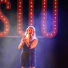 Pla mitjà de la cantant Suu amb el nom del grup de fons durant el seu concert al Festival Acústica de Figueres el 29 d'agost de 2019