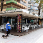 Plano abierto de una mujer paseando un perro cerca de una terraza del paseo de Salou prácticamente sin clientes
