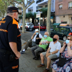 Dos voluntarios de Protección Civil controlando el uso de mascarilla entre varios vecinos de Reus sentados en un banco en el paseo Sunyer.