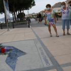 Tres dones observant unes flors i unes veles sobre el memorial commemoratiu dels atemptats terroristes, davant del Club Nàutic de Cambrils.