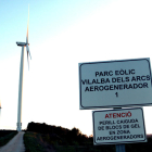Un cartel señalizando un parque eólico en Vilalba dels Arcs, en la Terra Alta, con dos aerogeneradores en el fondo.