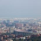 Barcelona amb el Camp Nou en primer pla i el port de fons amb boira per pol·lució al fons.