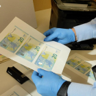 Un agente dels Mossos d'Esquadra sujetando billetes de 20 euros falsificados.