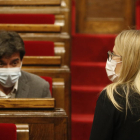 Pla del líder d'ERC al Parlament, Sergi Sabrià, assegut al seu escó del Parlament mentre la diputada i regidora de JxCat Elsa Artadi puja les escales de l'hemicicle
