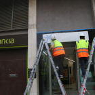 Una operarios cambiando los carteles de Bankia por los de CaixaBank en una oficina.