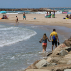 Una playa de Cunit sin arena, con dos bañistas cruzando con el agua en los tobillos.