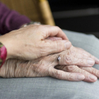 Primer plano de las manos cogidas de una cuidadora y una persona mayor con dependencia.
