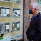Una persona mirant les ofertes de pisos a un aparador d'una immobiliària.