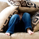 Imagen de recurso de un niño escondido entre cojines|almohadas en un sofá.