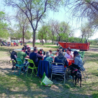 Un grup de familiars dinant al parc per a famílies i al seu darrere el contenidor amb les runes.