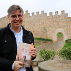 El escritor Jordi Nogués sujetando su nueva novela 'La rosa i la creu' delante de las murallas de Montblanc.