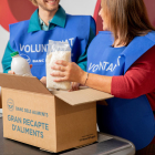 Imatge d'uns voluntaris del Banc dels Aliments guardant un paquet d'arròs i una ampolla de llet en una capsa.