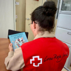 Una voluntària de Creu Roja d'esquenes subjectant un llibre.