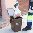 Pla tancat d'un operari traient una bossa d'escombraries del cubell de la fracció orgànica en una recollida porta a porta.