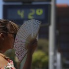 Una mujer se abanica junto a un termómetro de calle que marca 42 grados.