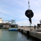 Una grua retira rodes i malles que un bussejador ha ajudat a agafar del fons marí del port de la Ràpita.