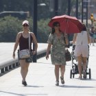 Una dona es protegeix del sol amb un paraigua i una altra amb una gorra, mentre caminen pel pont Vell de Lleida.
