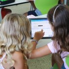 Dues nenes de Primària treballen amb una tauleta dins l'aula