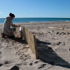 Una investigadora de la UdG col·loca un cartell informatiu en un dels captadors eòlics de la platja de Calafell.
