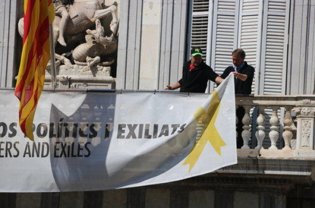 Dos treballadors retiren les pancartes del balcó del Palau de la Generalitat.