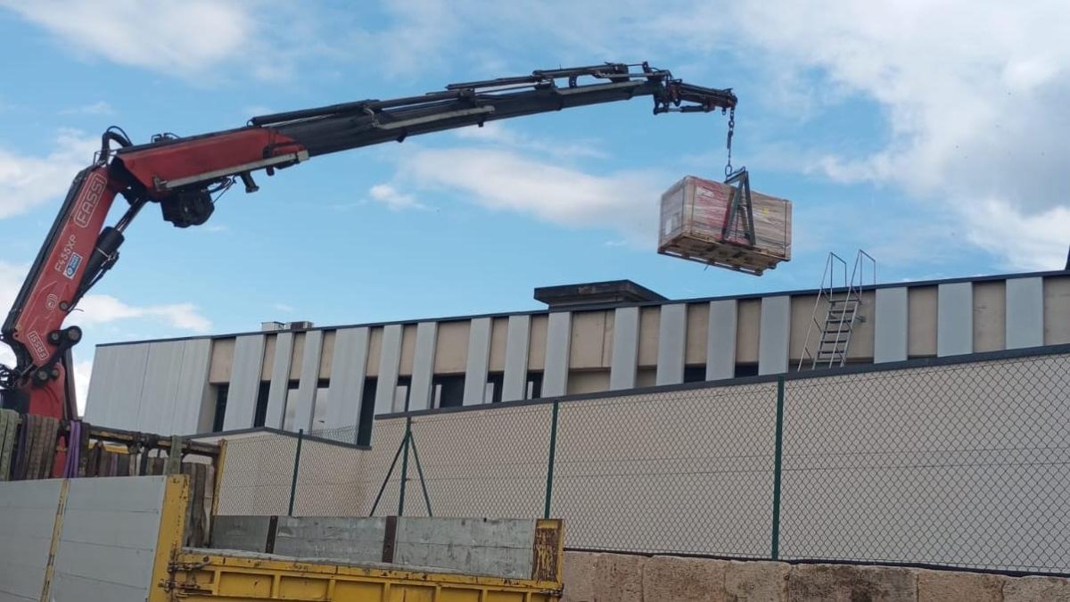 Una grua col·loca els panells solars al sostres de l'edifici de la Policia Portuària per a la seva instal·lació.