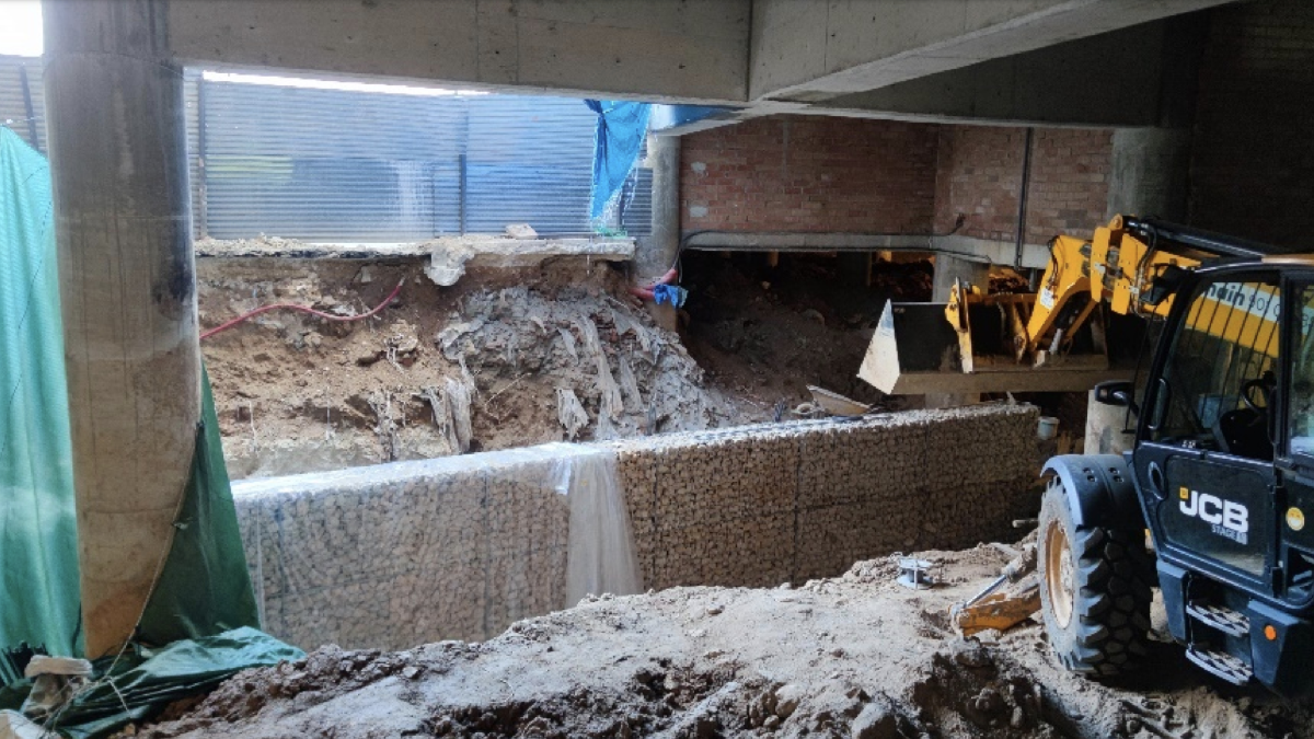 matge de la retroexcavadora a sobre de les restes de la Font dels Lleons, tapada per tones de terra. Al davant, el nou mur de contenció
