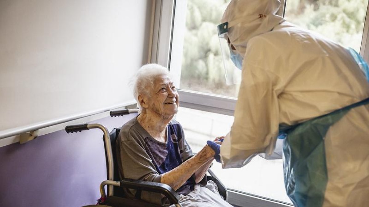 Una anciana con una enfermera con el EPI durante la pandemia covid-19.