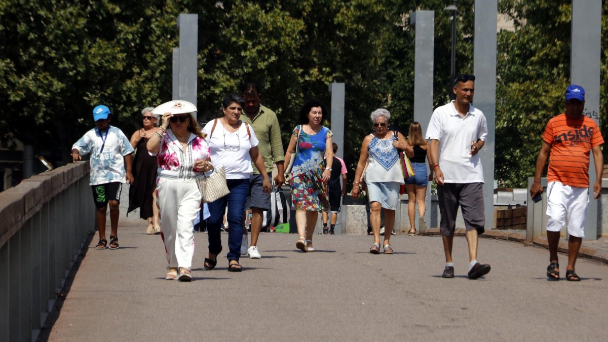 Peatones caminan protegiéndose del calor con abanicos y gorras.