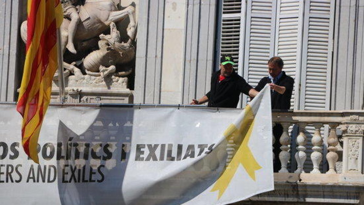 Dos treballadors retiren les pancartes del balcó del Palau de la Generalitat.
