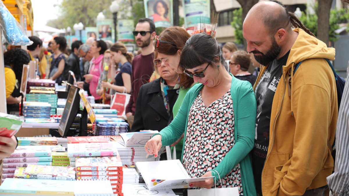 Varias personas hojean libros durante la Diada de Sant Jordi en la Rambla Nova de Tarragona.