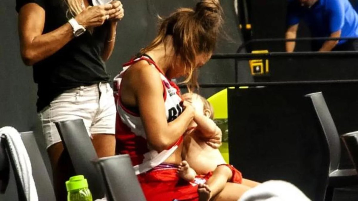 Una jugadora de baloncesto le da el pecho a su hija durante un partido