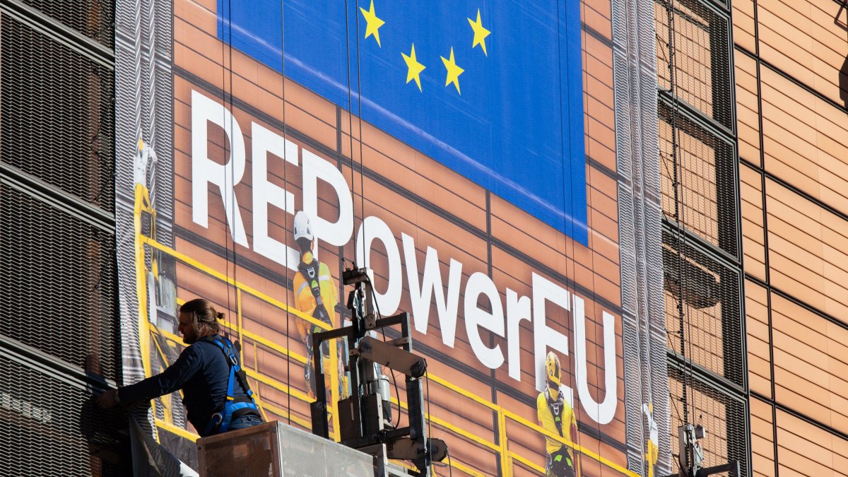 Un operario en la sede de la Comisión Europea coloca una lona anunciando el plan REPowerEU.