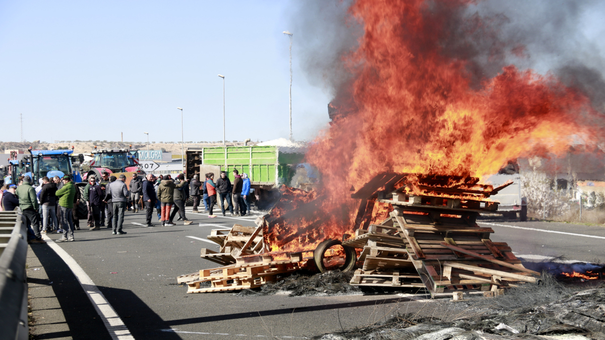 Una foguera amb manifestants i tractors al fons a l'A-2 a Tàrrega en el segon dia de protestes de la pagesia.