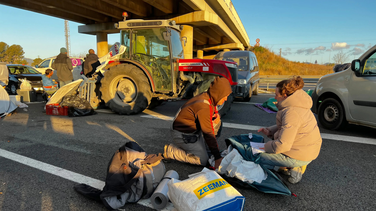 Dos manifestantes recogen la tienda de campaña después de haber pasado la noche cortante el AP-7 en Cambrils.