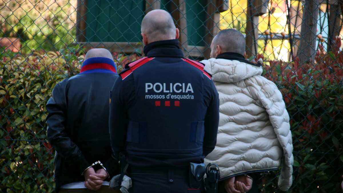 Un agent dels Mossos custodiant dos detinguts en l'operatiu per tràfic de drogues i falsificació de moneda.