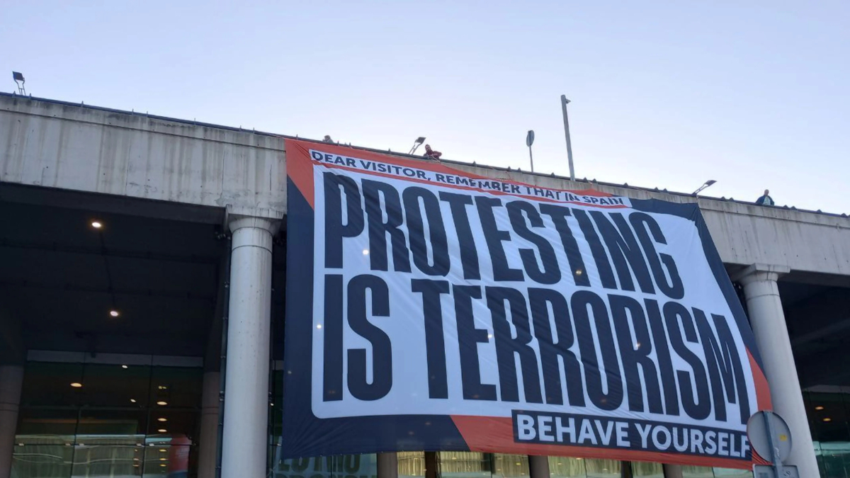 Òmnium despliega una pancarta gigante en el aeropuerto del Prat con el lema: 'En España, protestar es terrorismo'
