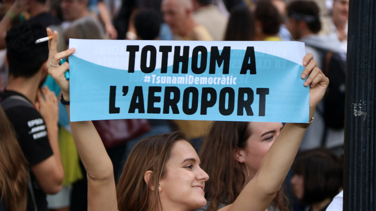 Una chica muestra un cartel de Tsunami Democrático llamando a la gente a movilizarse en el aeropuerto.