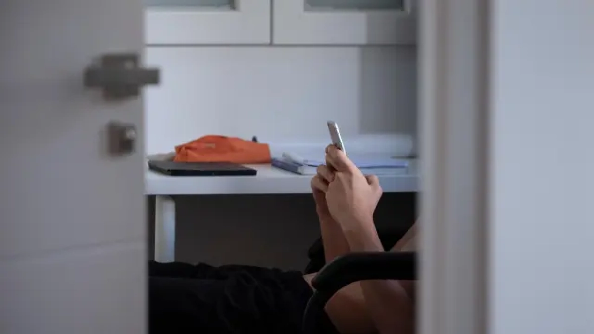 Adolescente mirando su teléfono móvil en la habitación.