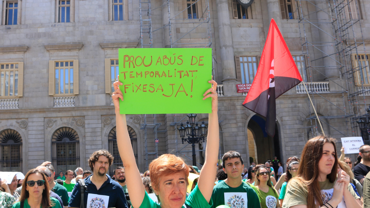 ¡Un manifestante alza un cartel con el mensaje «Bastante abuso temporalidad, fijeza ya»! a la protesta de interinos en la plaza de Sant Jaume