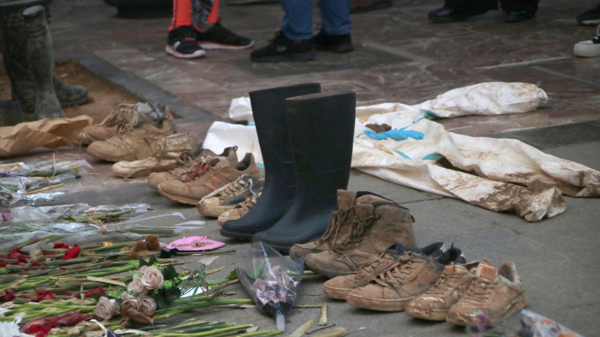 Zapatillas deportivas y botas manchadas de barro y flores, en un mural improvisado delante del Ayuntamiento de Valencia.