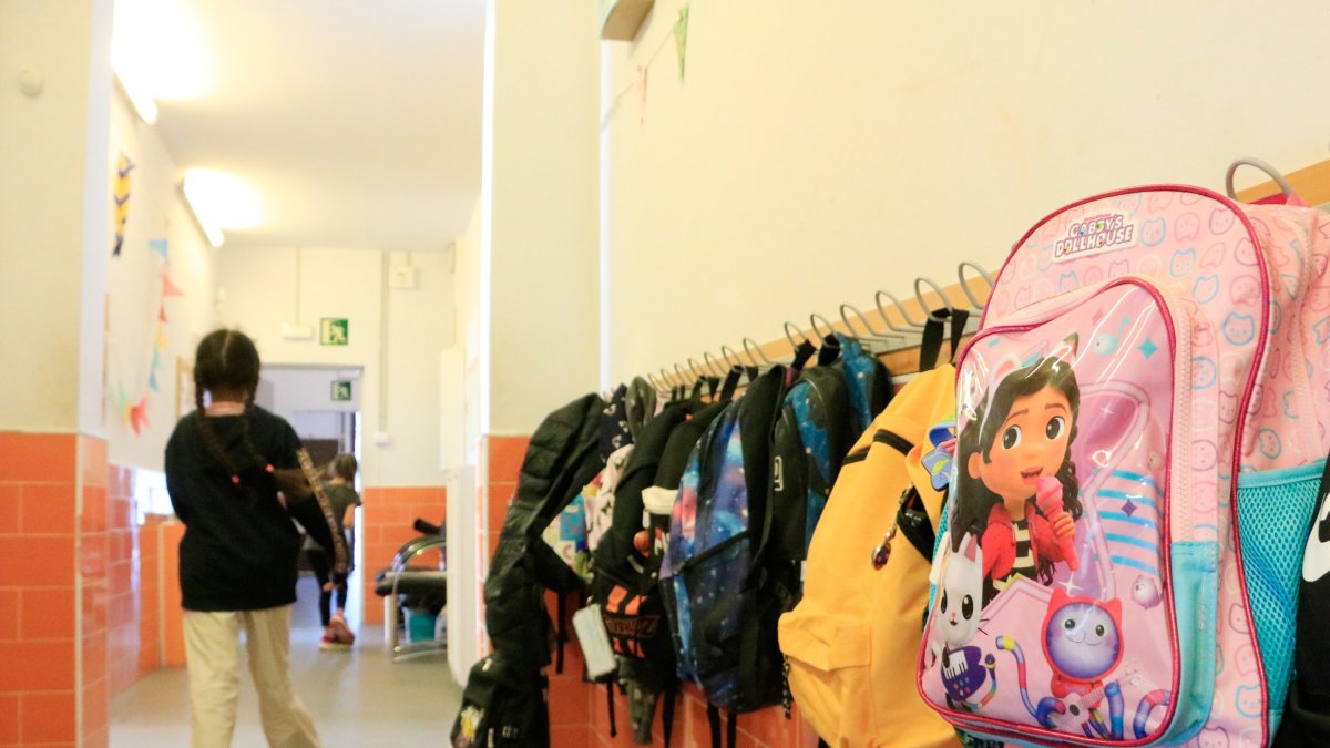 Una niña camina por el pasillo de una escuela, con las mochilas de los niños en las perchas.