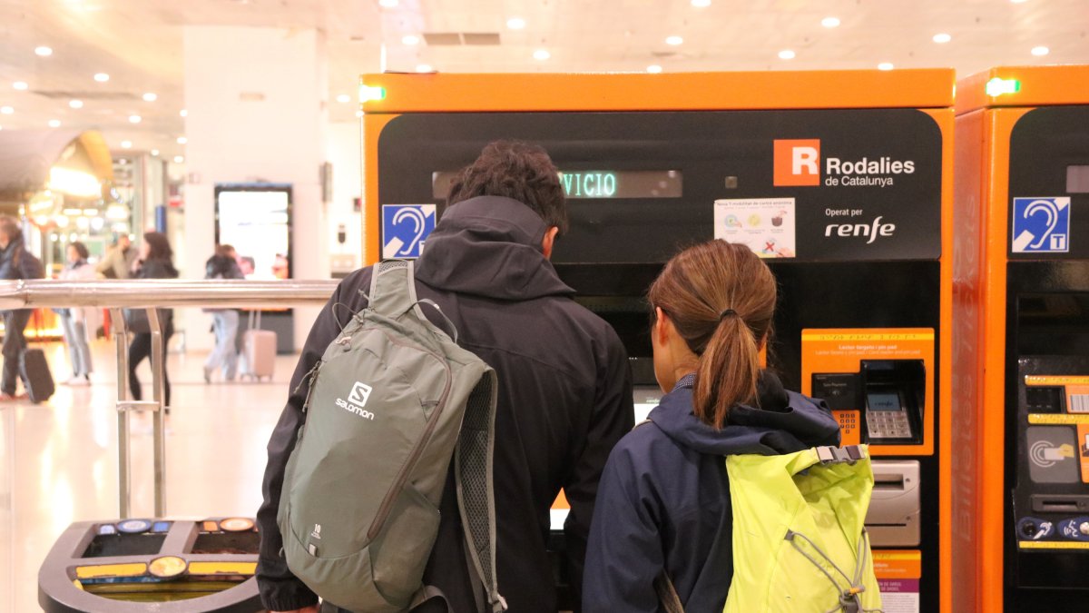 Dos personas comprando un billete de Rodalies en la estación de Sants