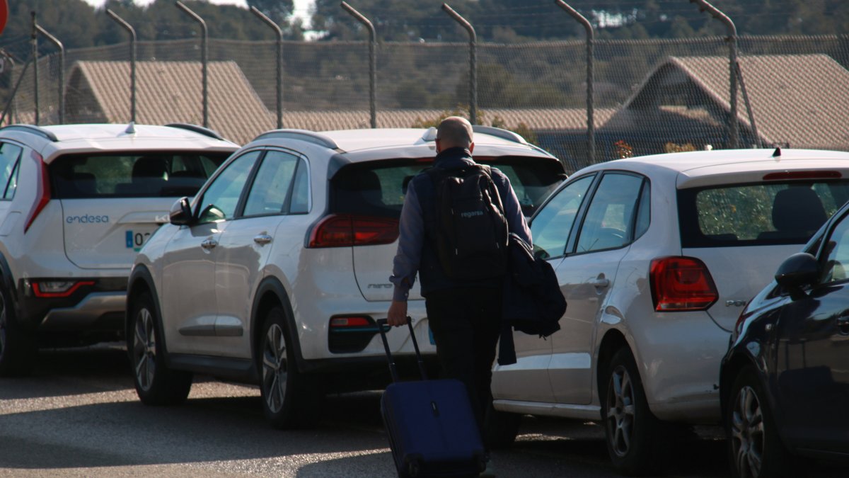 Un hombre con una maleta caminando por los arcenes de la entrada de la estación del Camp de Tarragona después de aparcar su vehículo.