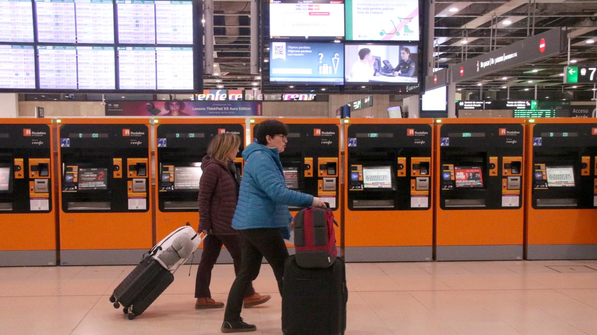 Dues persones amb maletes pel vestíbul de l'estació de Sants.